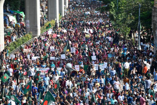 A crowd of protesters marches with flags, placards and