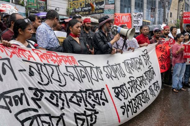 Protesters hold a banner, placards and chant slogans during